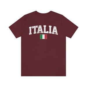 May include: A maroon t-shirt with the word "ITALIA" in white distressed lettering and the Italian flag printed below it.