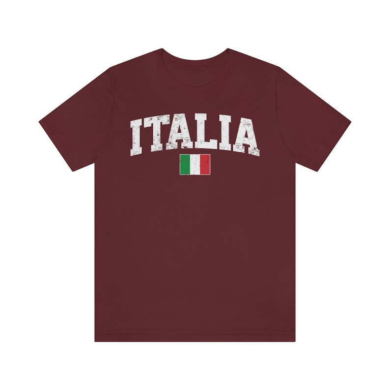 May include: A maroon t-shirt with the word "ITALIA" in white distressed lettering and the Italian flag printed below it.
