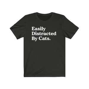 Może przedstawiać: Czarny T-shirt z białym tekstem, kt&oacute;ry brzmi "Easily Distracted By Cats."