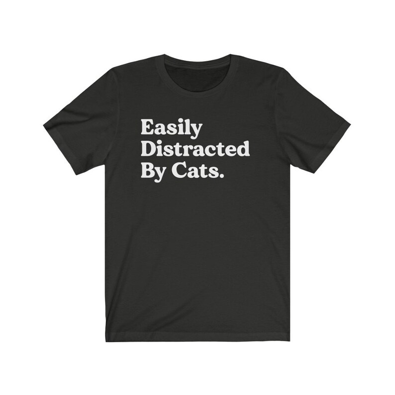 Może przedstawiać: Czarny T-shirt z białym tekstem, kt&oacute;ry brzmi "Easily Distracted By Cats."