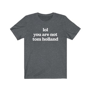 May include: A dark heather grey t-shirt with the text "lol you are not tom holland" printed in white.