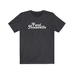 May include: A dark heather grey t-shirt with the text "Feral Housewife" printed in white.