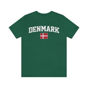K&ouml;nnte beinhalten: Ein gr&uuml;nes T-Shirt mit dem Wort "DENMARK" in wei&szlig;er, abgenutzter Schrift und der d&auml;nischen Flagge in Rot und Wei&szlig;.