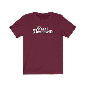 May include: Burgundy short-sleeved t-shirt with white text that reads "Feral Housewife".