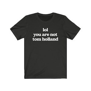 May include: Black t-shirt with white text that reads "lol you are not tom holland".