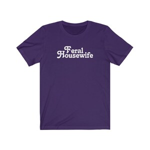 May include: Purple short-sleeved t-shirt with white text that reads "Feral Housewife".