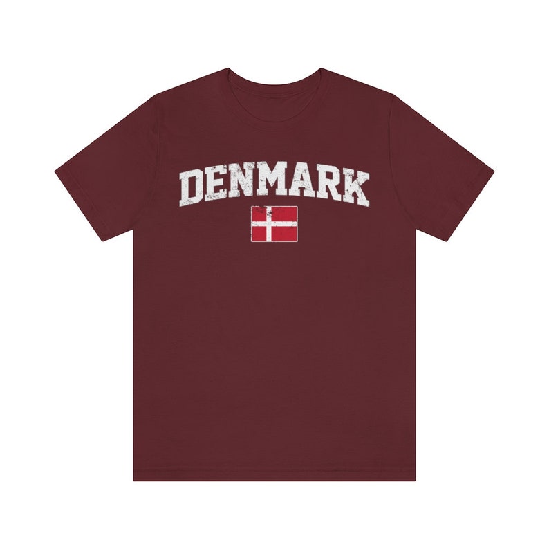 K&ouml;nnte beinhalten: Ein maroonfarbenes T-Shirt mit einem wei&szlig;en, abgenutzten Aufdruck des Wortes "DENMARK" und der d&auml;nischen Flagge.