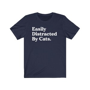 Może przedstawiać: Koszulka w kolorze granatowym z białym napisem "Easily Distracted By Cats."