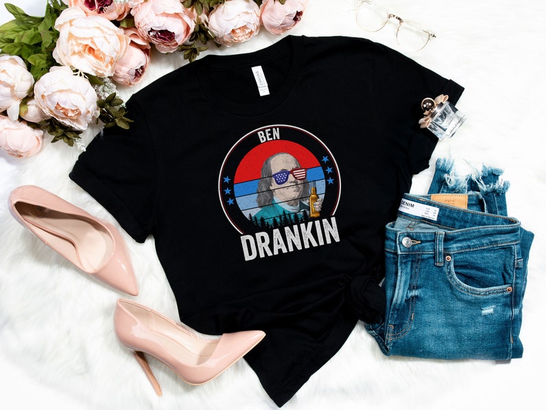 Puede incluir: Camiseta negra con un gr&aacute;fico de Ben Franklin con gafas de sol y sosteniendo una cerveza. El gr&aacute;fico est&aacute; en un c&iacute;rculo con el texto "Ben Drankin" debajo.