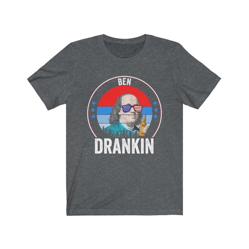 Puede incluir: Una camiseta gris oscuro jaspeada con un gr&aacute;fico de estilo vintage de Benjamin Franklin con gafas de sol y sosteniendo una cerveza. El gr&aacute;fico est&aacute; rodeado de estrellas y el texto "BEN DRANKIN".