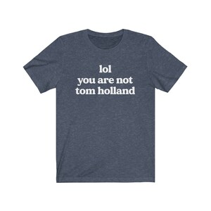 May include: A dark blue t-shirt with white text that reads "lol you are not tom holland".