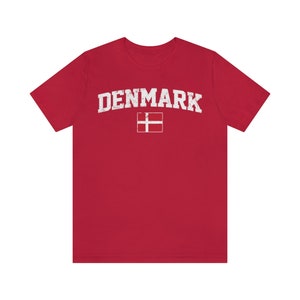 K&ouml;nnte beinhalten: Rotes T-Shirt mit einem wei&szlig;en, abgenutzten Aufdruck des Wortes "DENMARK" und der d&auml;nischen Flagge.