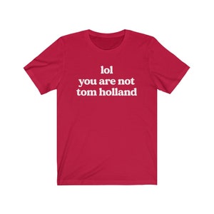 May include: Red short-sleeved t-shirt with white text that reads "lol you are not tom holland".