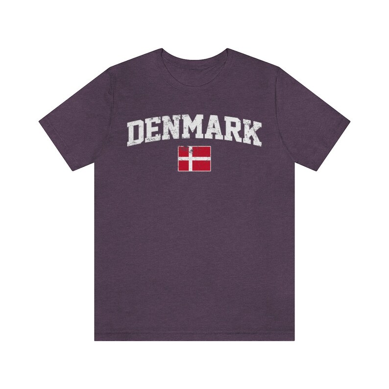 K&ouml;nnte beinhalten: Ein lila T-Shirt mit dem Wort "DENMARK" in wei&szlig;er, abgenutzter Schrift und der d&auml;nischen Flagge darunter.