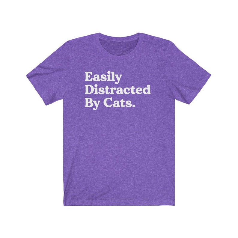 Może przedstawiać: Fioletowy T-shirt z kr&oacute;tkim rękawem z napisem "Easily Distracted By Cats." w kolorze białym.