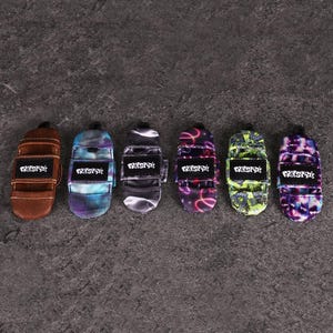 May include: Six small, rectangular, padded protective covers for roller skate toe stops, each featuring a black label with the white text "FREESTYLE". The covers come in various colors and patterns, including brown, blue tie-dye, black, pink, green, and purple.