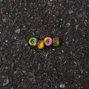 May include: Four colorful skateboard wheels with black, yellow, green, and pink accents. The wheels are on a dark gray asphalt surface.