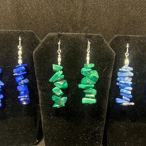 May include: Three pairs of dangle earrings with silver hooks. Each pair features a different gemstone: blue lapis lazuli, green malachite, and blue lapis lazuli.