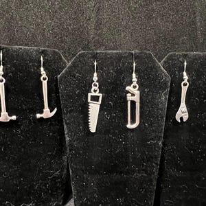 Könnte beinhalten: Sechs Paar silberne Ohrringe mit verschiedenen Werkzeugen, darunter ein Hammer, eine Säge, ein Schraubenschlüssel und eine Zange.