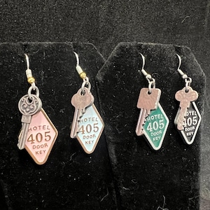 May include: Three pairs of silver key earrings with a diamond-shaped tag that says "HOTEL 405 DOOR KEY". The tags are pink, green, and blue.