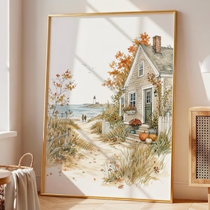 May include: A framed watercolour-style print depicting a coastal cottage during autumn. The scene features a sandy path leading to the ocean, a lighthouse in the distance, orange-hued trees, and pumpkins on the porch of the house.