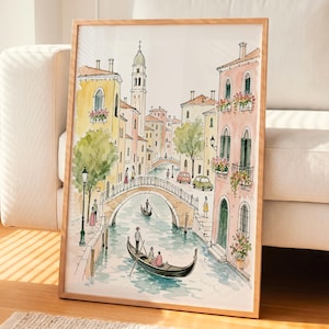 May include: A framed watercolor print depicting a canal scene in Venice with yellow and pink buildings, a stone arched bridge, and a gondola with passengers on the water. The illustration features green trees, small cars, and people walking.