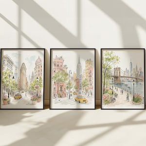 May include: A set of three framed watercolor prints depicting New York City scenes. The first shows the Flatiron Building, the second a city street with brownstones, and the third the Brooklyn Bridge with a waterfront park, all in soft tones.