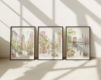 May include: A set of three framed watercolor prints depicting New York City scenes. The first shows the Flatiron Building, the second a city street with brownstones, and the third the Brooklyn Bridge with a waterfront park, all in soft tones.