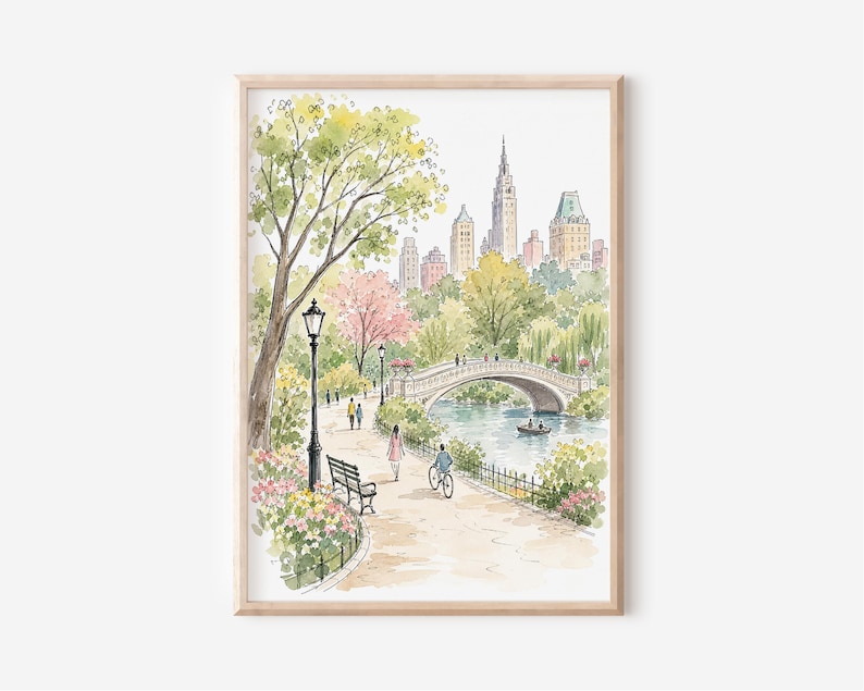 May include: A framed watercolor print depicting a park scene with a stone bridge over a pond, a winding path, a black lamppost, a bench, and people walking or cycling. In the background, a city skyline rises above lush green and pink trees.