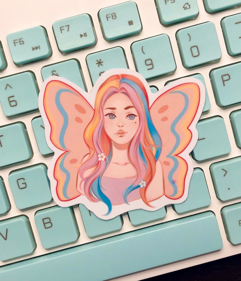May include: A sticker featuring a colorful illustration of a person with butterfly wings. The person has long, pink, blue, and yellow hair and is wearing a light pink shirt. The butterfly wings are pink, blue, and yellow.
