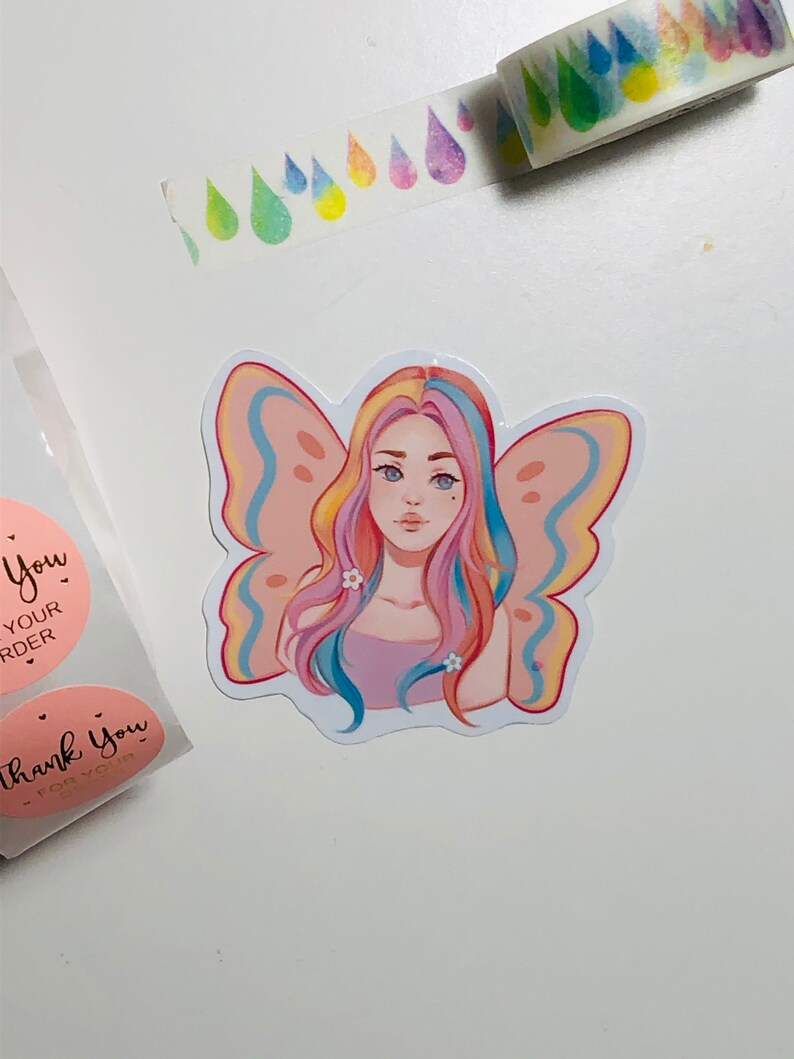 May include: A sticker featuring a colorful illustration of a girl with rainbow hair and butterfly wings. The girl is wearing a pink top and has white flowers in her hair. The sticker is on a white background.