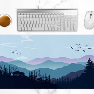 Könnte beinhalten: Schreibtischunterlage mit einem Berglandschaftsdesign in Blau- und Lilatönen. Ein Haus liegt zwischen den Bäumen. Eine Vogelschar fliegt über den Himmel. Eine weiße Tastatur, Maus und Kaffeetasse sind ebenfalls sichtbar.