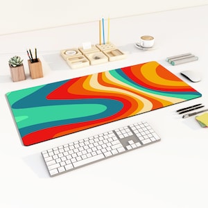 May include: A colorful desk mat with a wavy, abstract design in shades of red, orange, yellow, green, and blue. A white keyboard and a white mouse are on the desk mat.