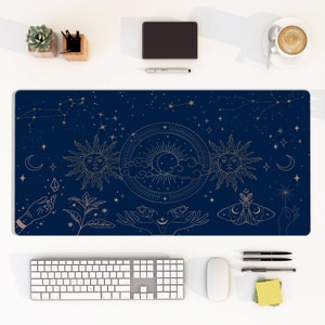 Puede incluir: Una alfombrilla de escritorio azul con un diseño celestial con estrellas, lunas y soles dorados. El diseño incluye un sol con cara, una luna creciente y un sol con una nube. La alfombrilla también presenta dos manos con una luna creciente entre ellas, una polilla y una mano sosteniendo una estrella.