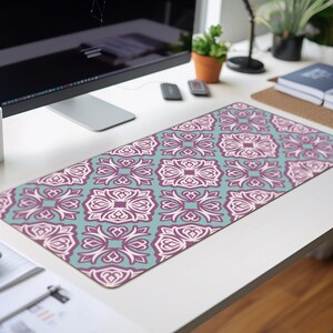 May include: A teal and purple patterned desk mat with a geometric design. The mat is on a white desk with a computer monitor, a laptop, and other office supplies.