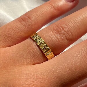 Pu&ograve; includere: Un anello d'oro con una superficie testurizzata. L'anello &egrave; indossato su un dito.