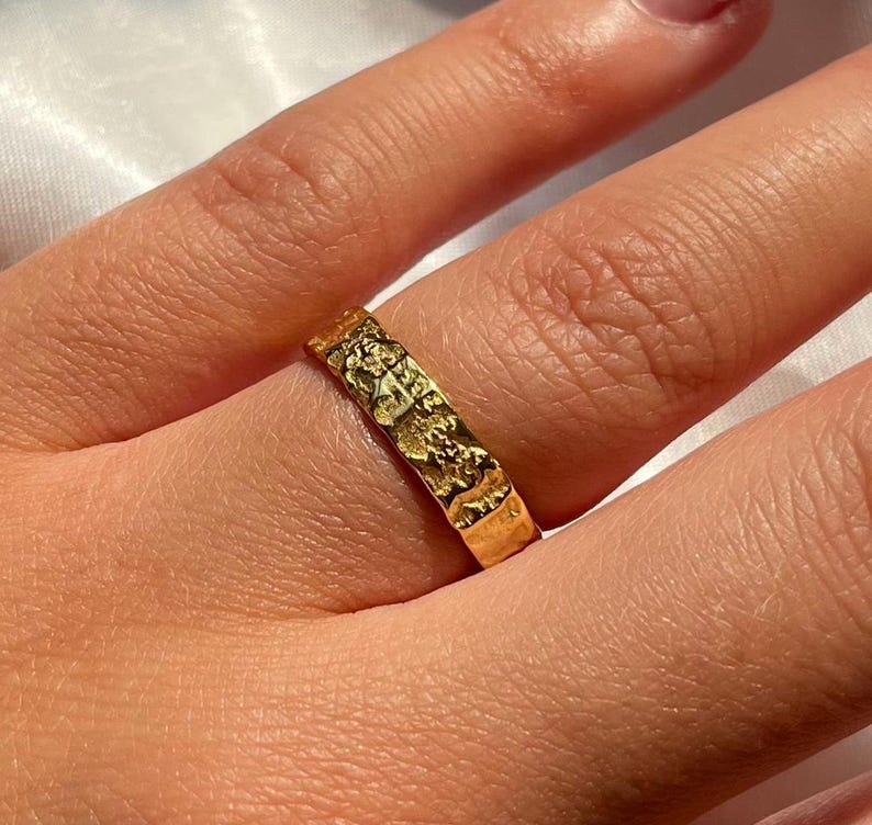 Pu&ograve; includere: Un anello d'oro con una superficie testurizzata. L'anello &egrave; indossato su un dito.