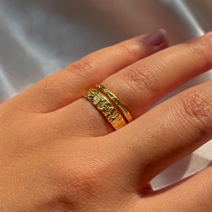 Pu&ograve; includere: Due anelli d'oro impilati su un dito. L'anello superiore &egrave; una semplice fascia, mentre l'anello inferiore ha un design testurizzato.