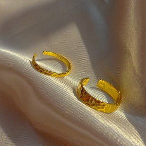 以下が含まれることがあります： テクスチャ加工されたハンマー仕上げのゴールドトーンのリング2つ。リングはオープンで調節可能です。