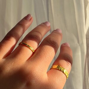 Pu&ograve; includere: Due anelli d'oro su una mano. Un anello &egrave; una fascia sottile, l'altro &egrave; una fascia pi&ugrave; spessa con una superficie testurizzata.