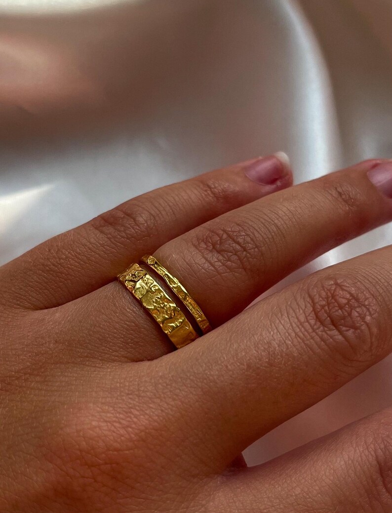Pu&ograve; includere: Due anelli d'oro impilati su un dito. L'anello superiore &egrave; una fascia sottile con una texture martellata. L'anello inferiore &egrave; pi&ugrave; largo e ha una texture martellata pi&ugrave; intricata.