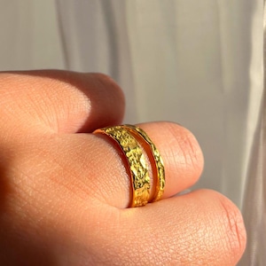 Pu&ograve; includere: Due anelli in metallo martellato color oro impilati su un dito.