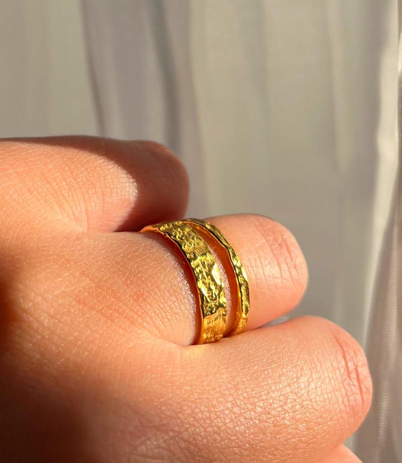 Pu&ograve; includere: Due anelli in metallo martellato color oro impilati su un dito.