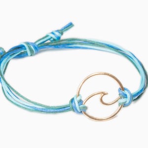 May include: A blue and green braided cord bracelet with a gold wave charm.
