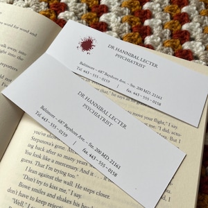 May include: Two business cards for Dr. Hannibal Lecter, a psychiatrist. The cards are white with black text and a red blood splatter on the top card. The text on the cards includes the name, title, address, phone number, and fax number.