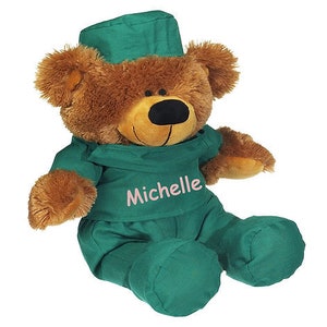 May include: A brown teddy bear wearing a green doctor's uniform and a green hat. The bear has a pink embroidered name "Michelle" on the uniform.