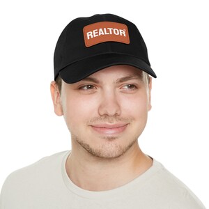 May include: A black baseball cap with a brown leather patch that says "REALTOR®" in white text.