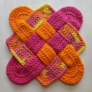 May include: A crocheted pot holder in a woven design with pink, orange, and yellow ombre yarn.
