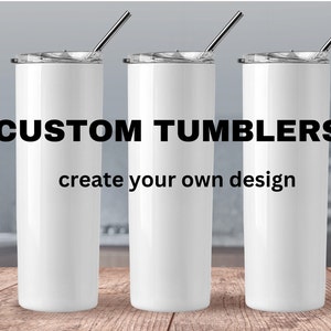 May include: Three white stainless steel tumblers with lids and straws. The tumblers are on a wooden surface. The text "CUSTOM TUMBLERS create your own design" is displayed in black letters on a white background.