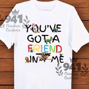 May include: White t-shirt with a colorful graphic of Toy Story characters spelling out "You've Got a Friend in Me".